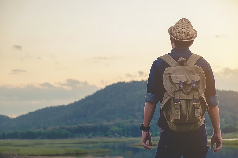 Jeune randonneur au coucher de soleil portant un sac à dos en toile cirée